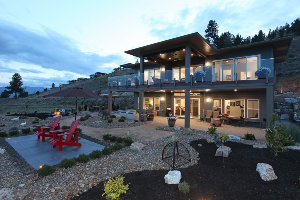 View of the front side and yard of the Keech residence at dusk, with interior and exterior lights on.