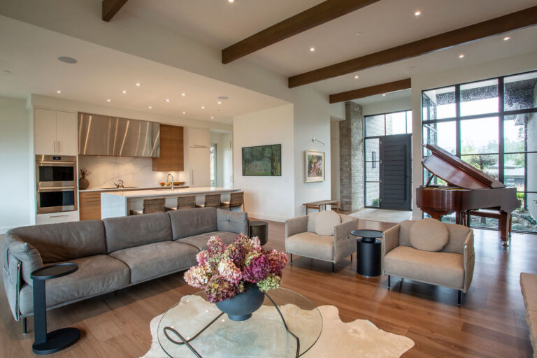 Open-concept living area with a modern kitchen in the background, featuring a large island with bar seating and a cozy seating arrangement.
