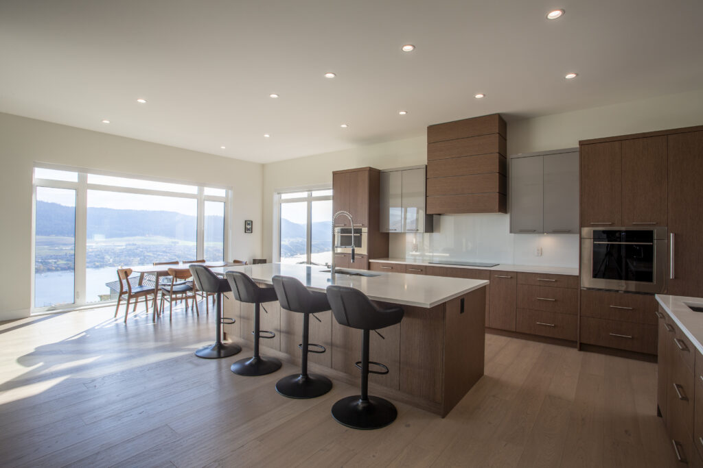 Bright, open kitchen featuring a large island with bar seating, wood cabinetry, and expansive windows offering a view of the surrounding landscape.