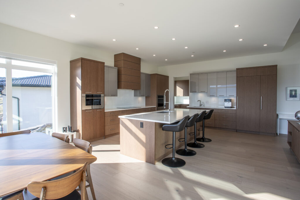 Open-concept kitchen and dining area with wood cabinetry, a large central island, and a dining table set near floor-to-ceiling windows.
