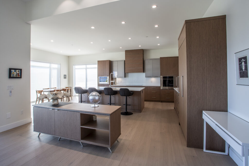 Spacious, modern kitchen with a large central island, wood cabinetry, and a dining area with large windows providing natural light.