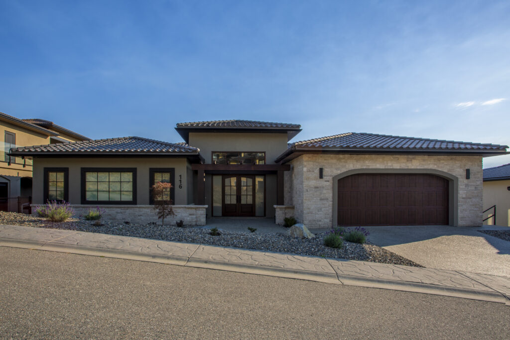 Front view of a modern, single-story home with a stone and stucco exterior, a tiled roof, and a landscaped front yard.