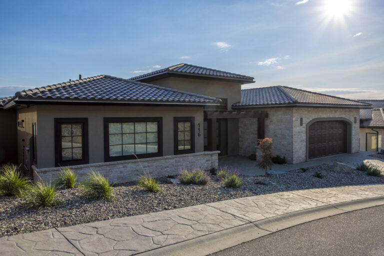 Exterior view of a modern, single-story home with a stone facade, tiled roof, and minimalist landscaping under a clear sky.