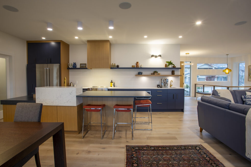 Spacious kitchen featuring blue and wood cabinetry, a central island with bar stools, and an open view to the living area, designed with modern and minimalist decor.