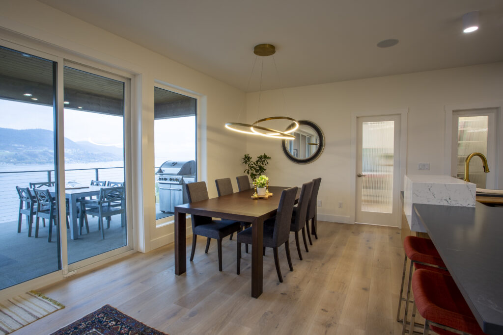 Dining area with a large wooden table, modern lighting, and sliding glass doors that open to an outdoor patio with views of the surrounding landscape.
