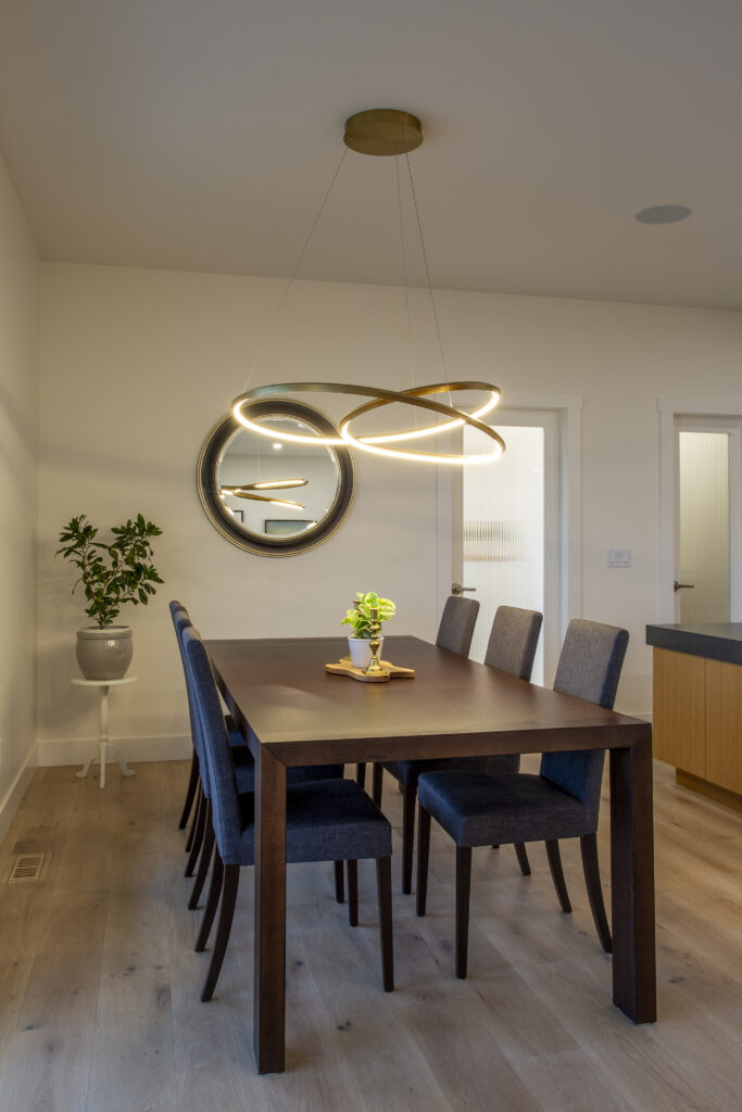 Alternate view of the dining area and kitchen, highlighting the modern lighting fixture, wooden dining table, and the spacious, open-concept layout.