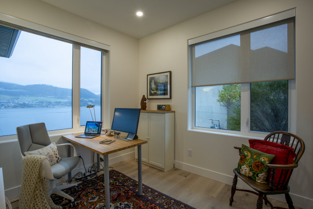 Home office with a desk and chair, large windows, and a view of the water outside.