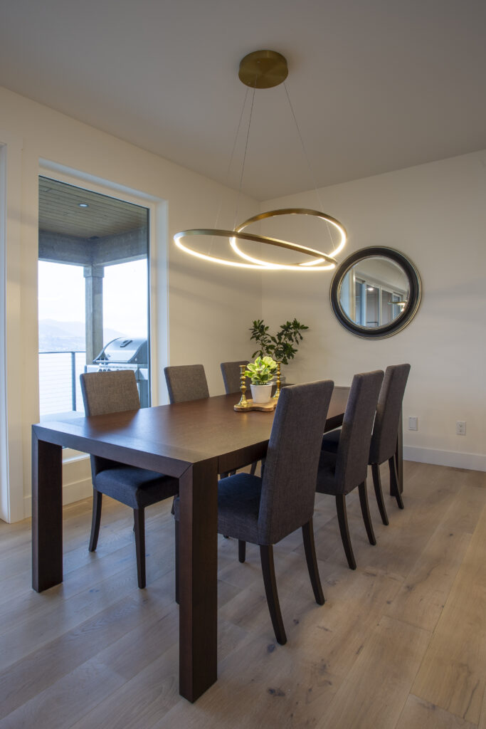 Dining area with a large wooden table, modern lighting, and sliding glass doors that open to an outdoor patio with views of the surrounding landscape.