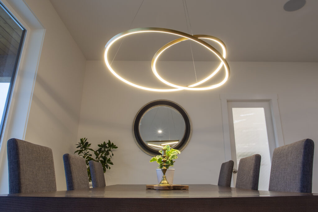 Dining area with a large wooden table, modern lighting, and sliding glass doors that open to an outdoor patio with views of the surrounding landscape.