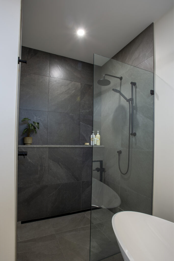 Shower area with large gray tiles, built-in shelf, and glass door.