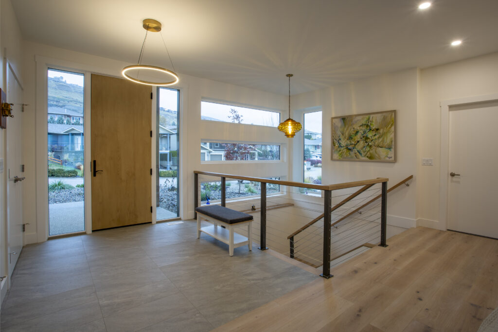 Entryway with a wooden front door, modern lighting, and staircase with glass railings.