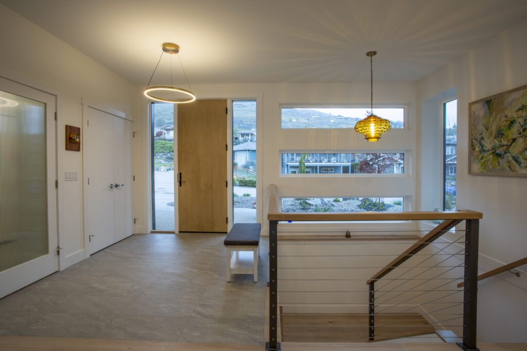 Entryway with a wooden front door, modern lighting, and staircase with glass railings.