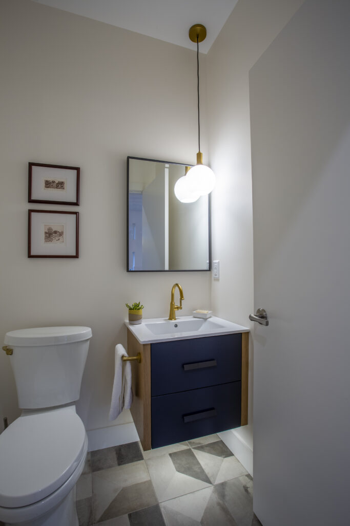 Modern bathroom with a navy blue vanity, brass fixtures, and round mirror.