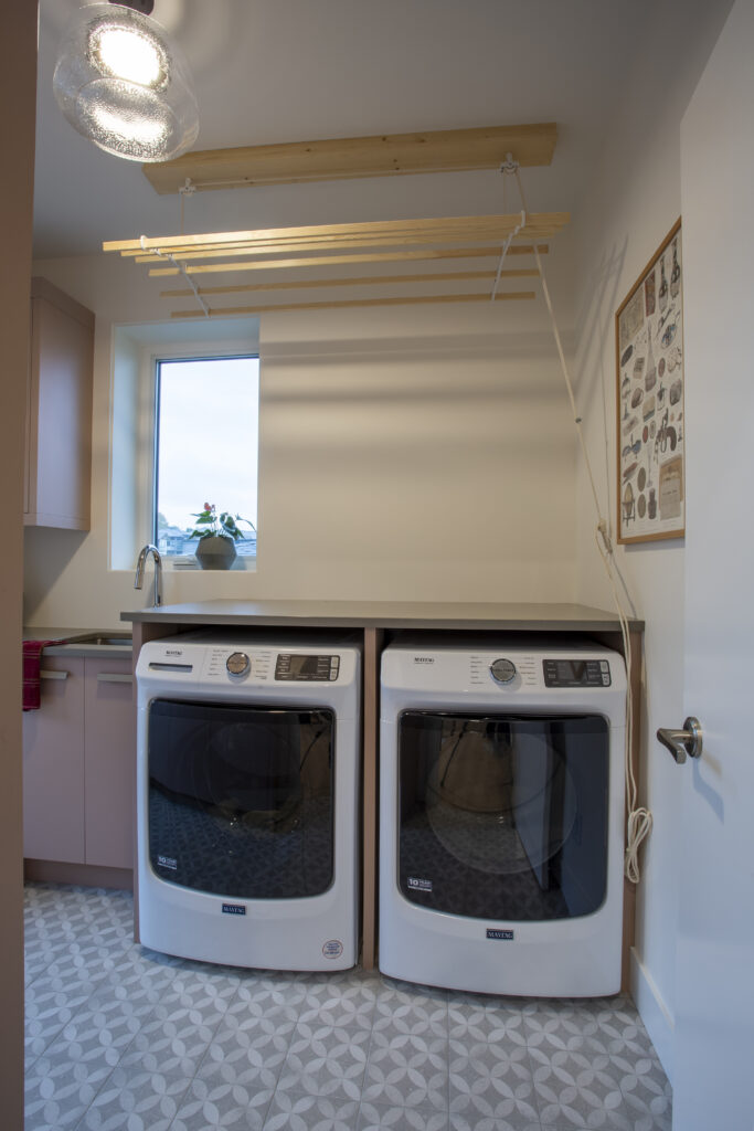 Laundry room with a washer and dryer, wooden countertop, and drying rack.