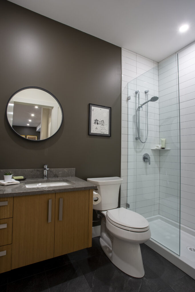 Modern bathroom with dark vanity, glass shower, and round mirror.
