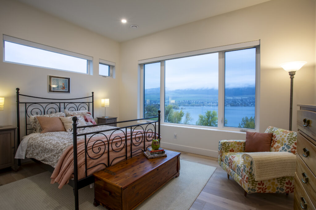 Bedroom with a metal bed frame, large windows overlooking a lake, and a floral armchair.