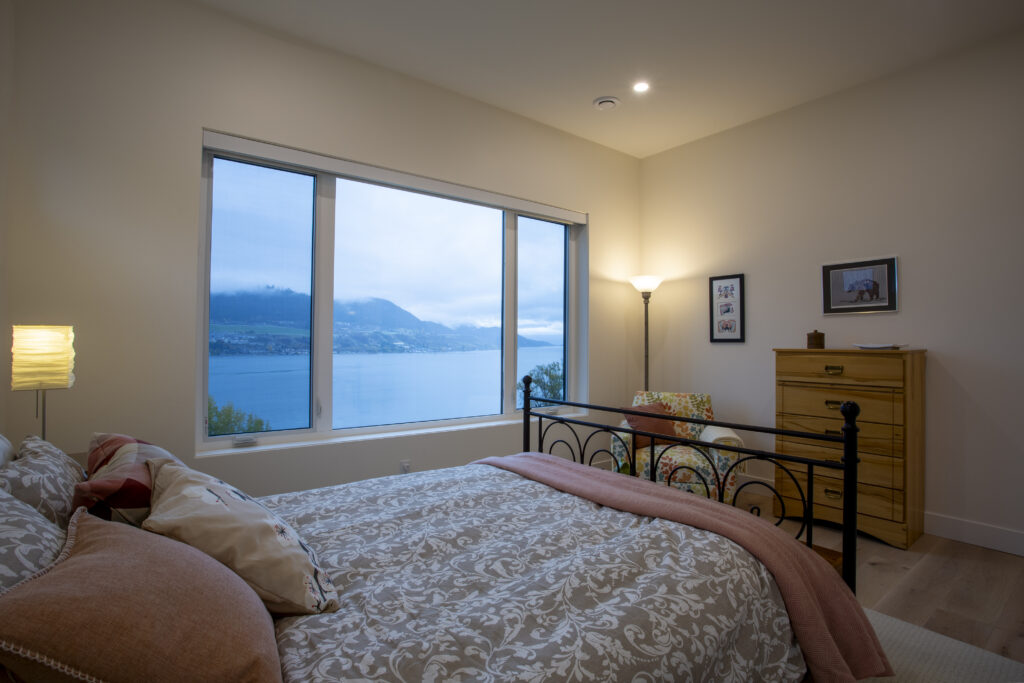 Bedroom with a metal bed frame, large windows overlooking a lake, and a floral armchair.