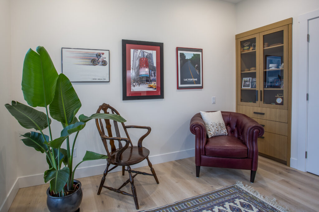 Reading nook with a wooden chair, red leather armchair, and framed artwork.