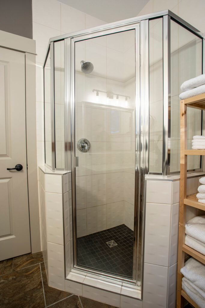 Luxury glass-enclosed shower with chrome finishes and white tiled walls in a Keith Construction home renovation.