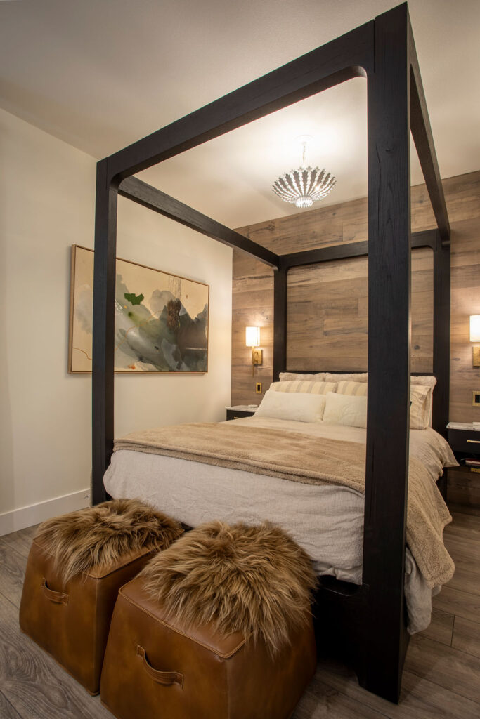 Close-up of a modern four-poster bed with soft neutral bedding, framed artwork, and warm wood paneling in a Keith Construction home.
