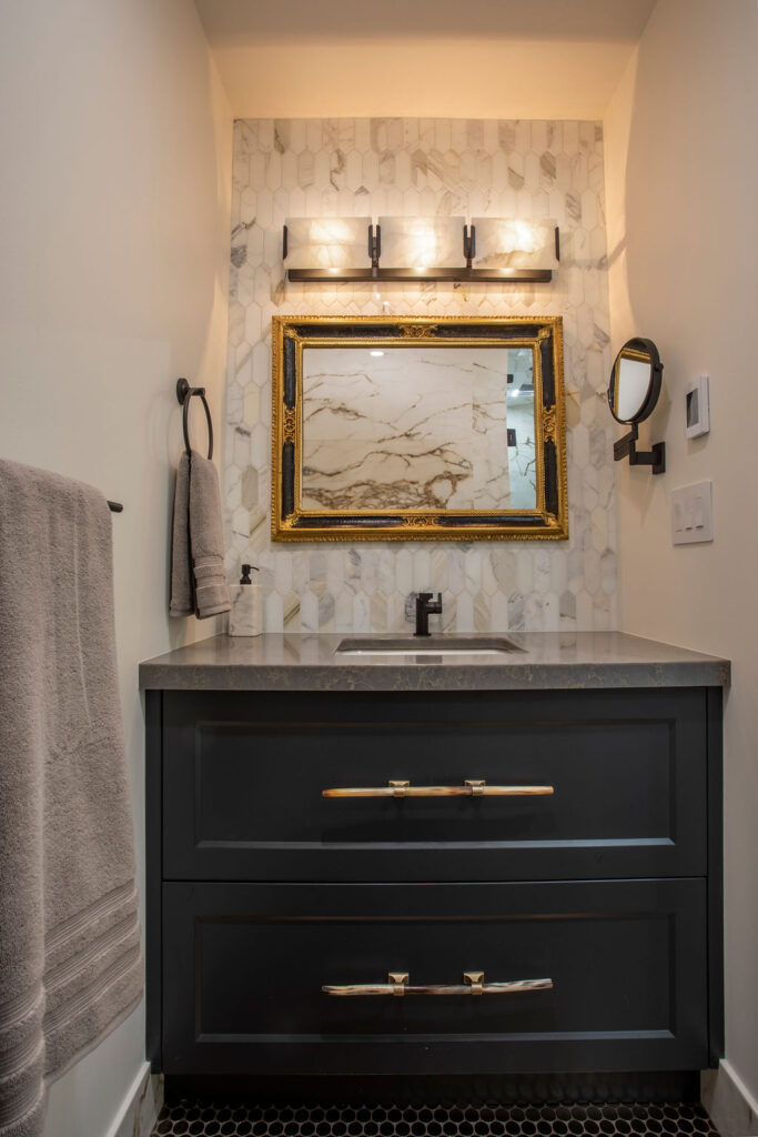 Elegant bathroom vanity with a marble backsplash, gold-framed mirror, and dark cabinetry in a Keith Construction home renovation.