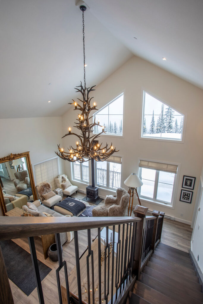 View from the upper level showing the living area with an antler chandelier and large windows.