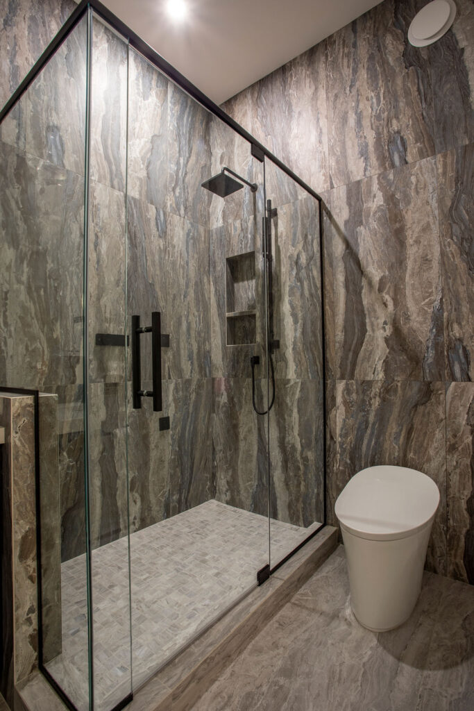 Modern bathroom with a glass shower enclosure, dark cabinetry, and hanging light fixtures.