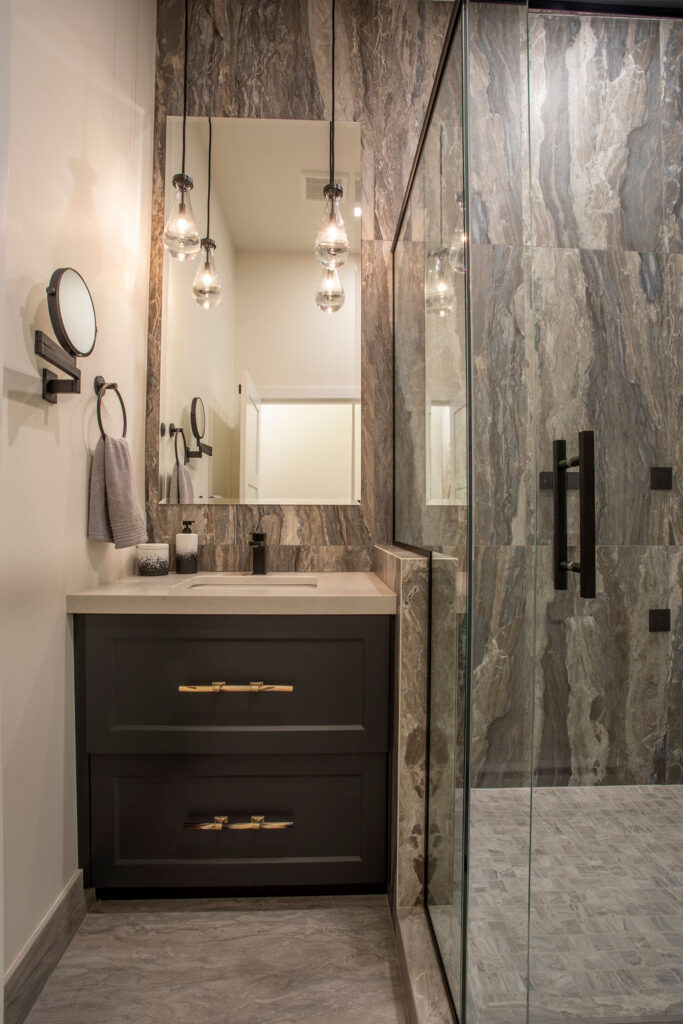 Modern bathroom with a glass shower enclosure, dark cabinetry, and hanging light fixtures.