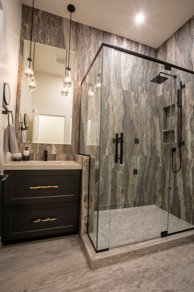 Modern bathroom with a glass shower enclosure, dark cabinetry, and hanging light fixtures.