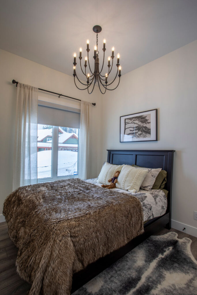 Cozy bedroom with a fur blanket, dark wooden bed frame, and a chandelier overhead.