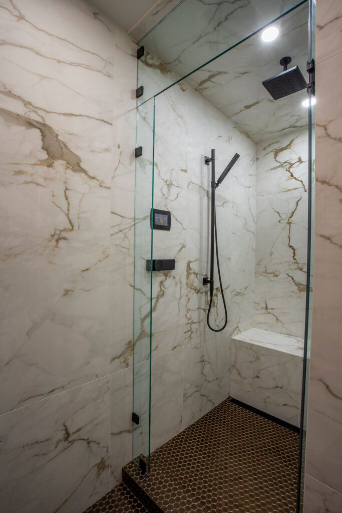 Modern bathroom with a glass shower enclosure, dark cabinetry, and hanging light fixtures.