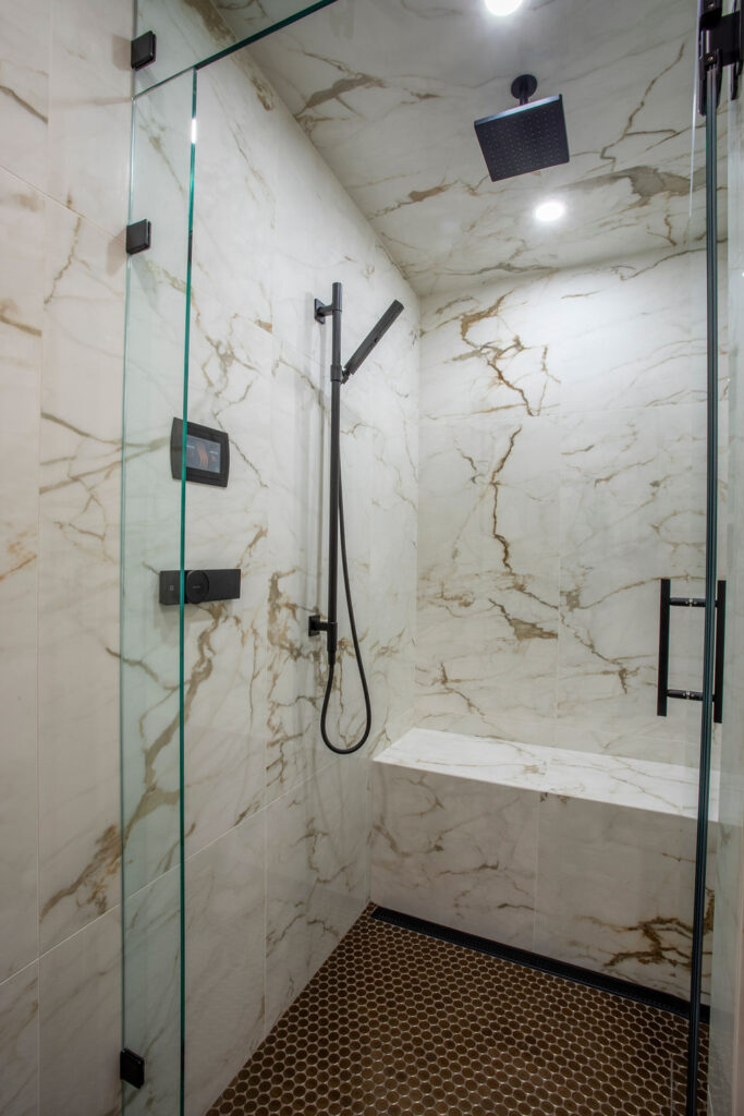 Modern bathroom with a glass shower enclosure, dark cabinetry, and hanging light fixtures.