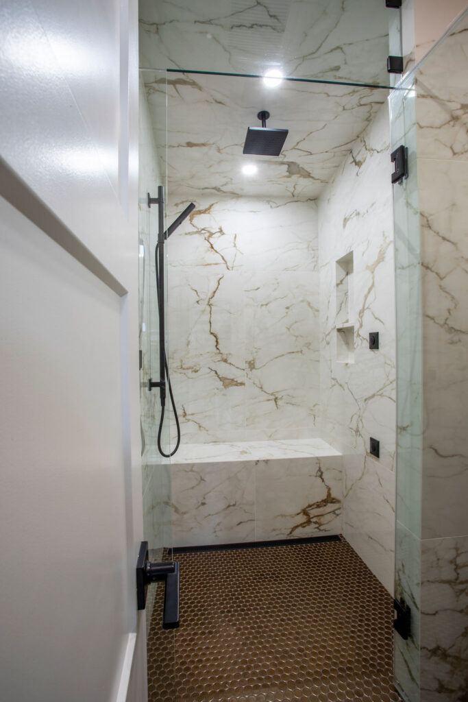 Modern bathroom with a glass shower enclosure, dark cabinetry, and hanging light fixtures.