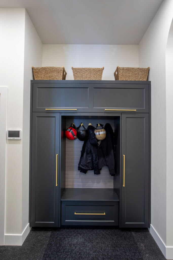 Mudroom storage unit with dark cabinetry, hooks, and wicker baskets on top.