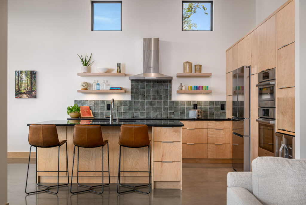 Contemporary kitchen with open shelving, birch wood cabinets, a black soapstone countertop, and a green tile backsplash.