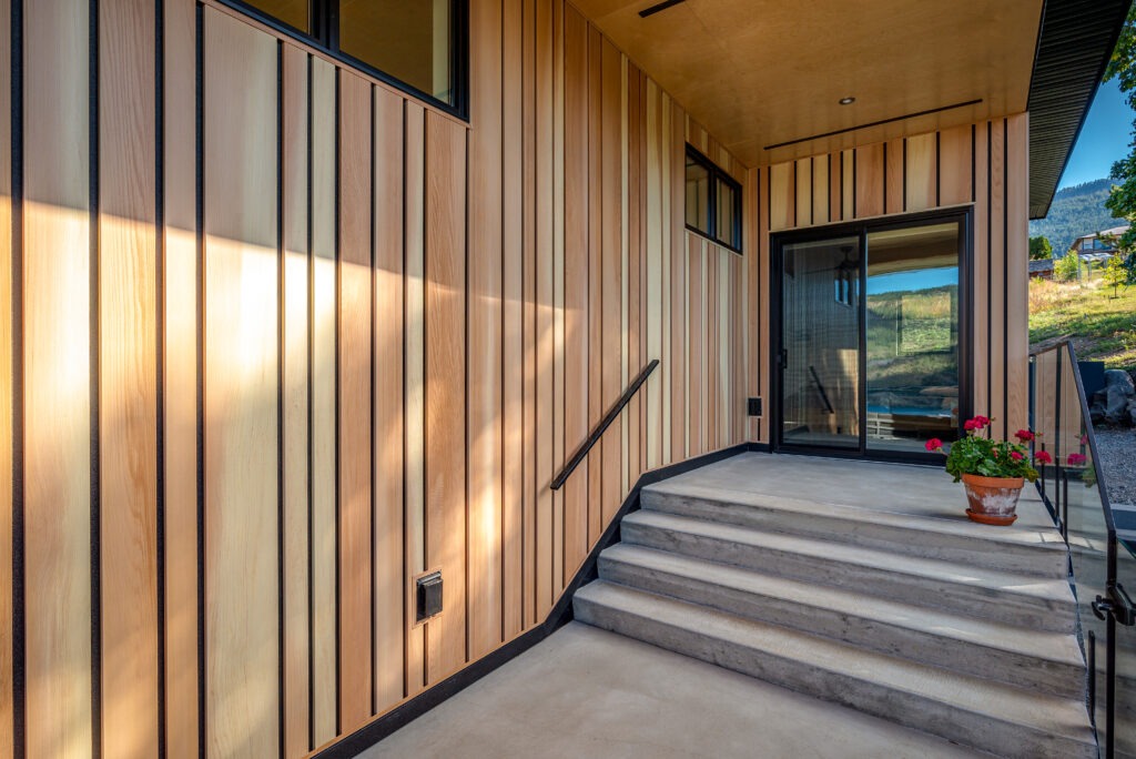 Covered side entrance of a custom-built home in Lake Country featuring vertical wood siding and modern black-framed windows.