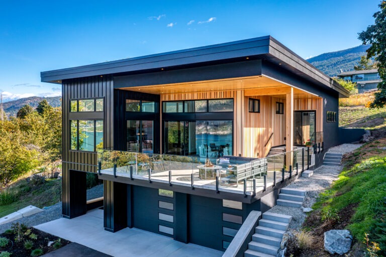 Modern Lake Country custom home with dark metal accents, wood siding, and an expansive glass balcony overlooking the landscape.