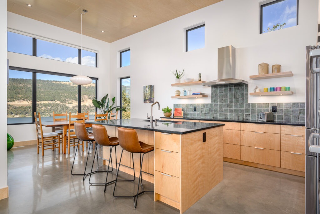 Open-concept kitchen and dining space with high ceilings, birch cabinets, large windows, and modern barstools.