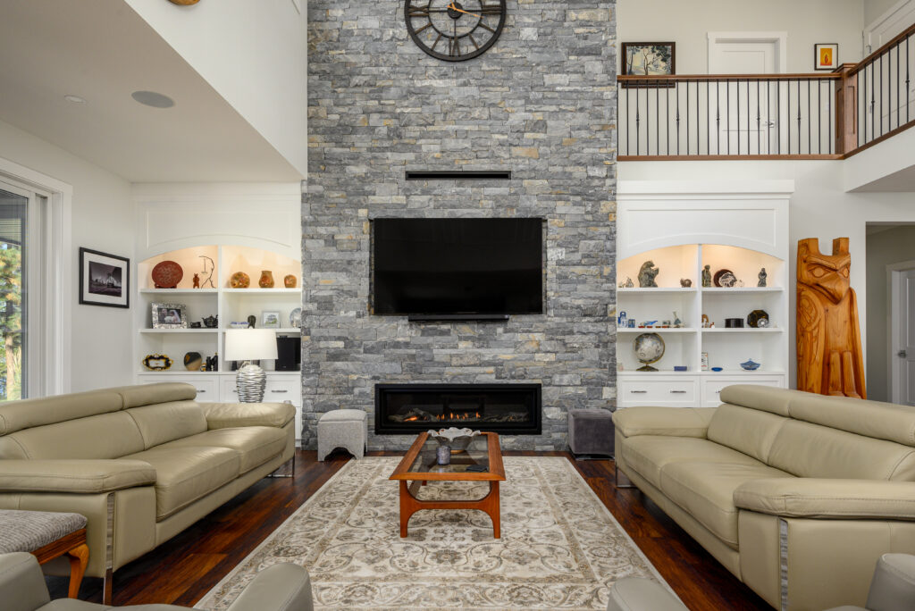Custom home living room in Lake Country with a floor-to-ceiling stone fireplace, vaulted ceilings and built-in shelving.