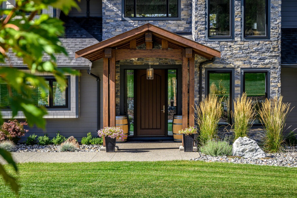 Timber-framed entrance of a custom home with natural stone details, surrounded by greenery.