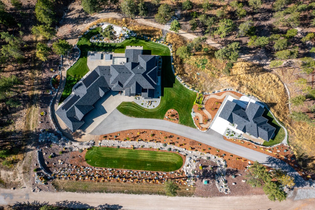 Aerial view of a custom home in Lake Country with a curved driveway, detached garage and lush landscaping surrounded by trees.