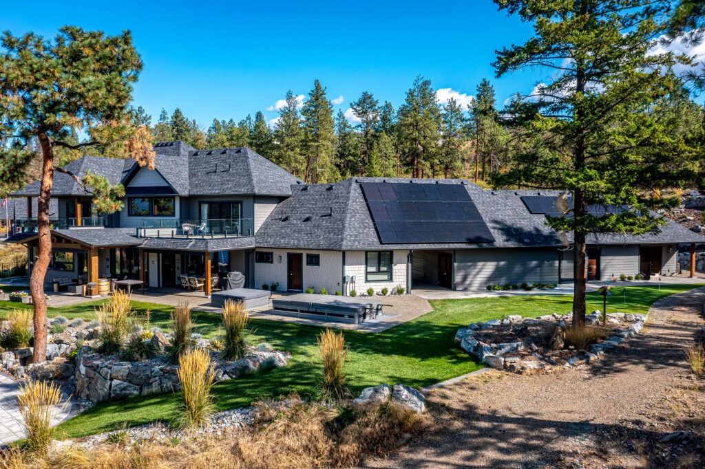 Rear view of a custom home in Lake Country featuring stone and wood finishes, glass doors and a landscaped yard.